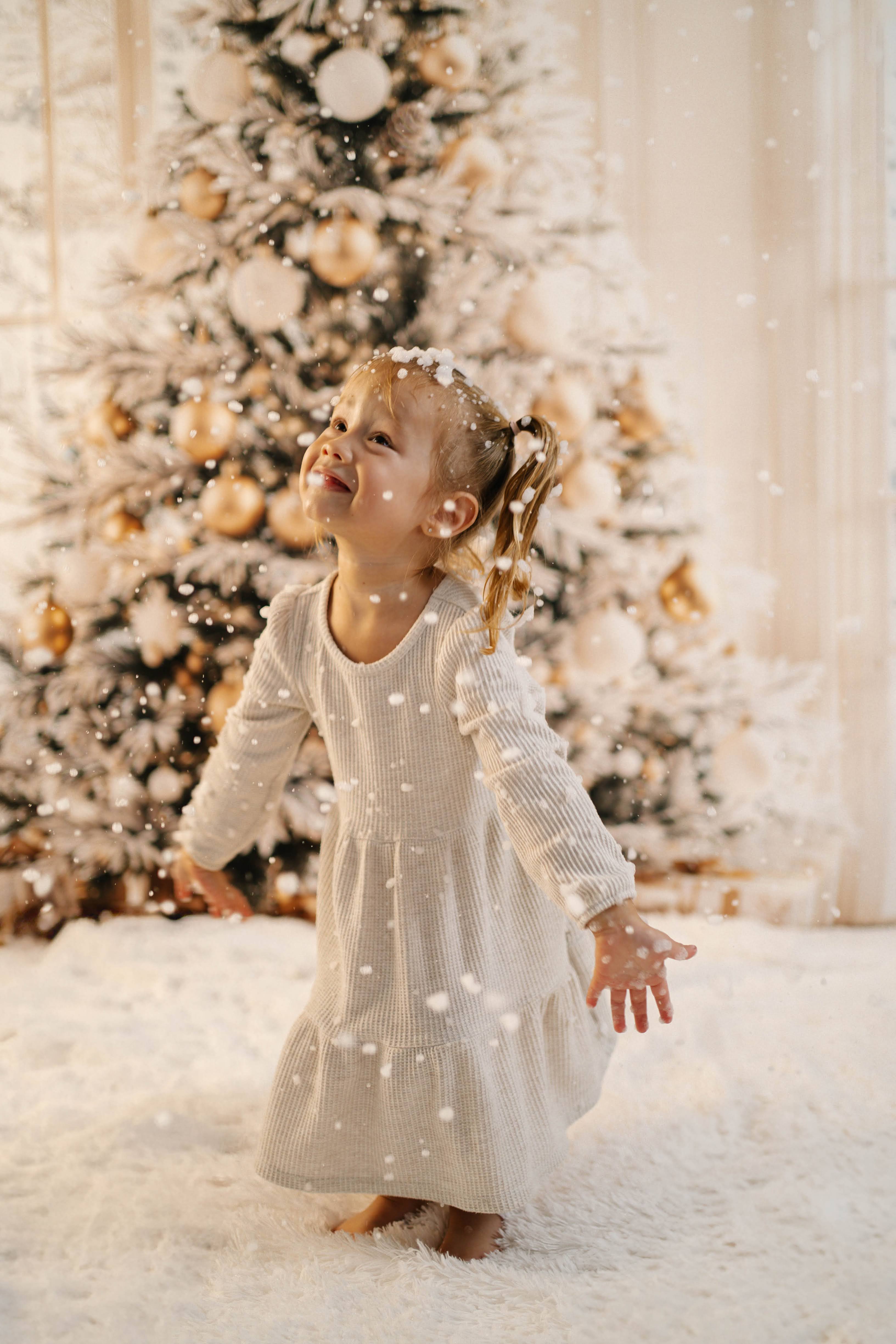 Child smiling in falling snow in front of a Christmas tree during a Vacaville family photography session.