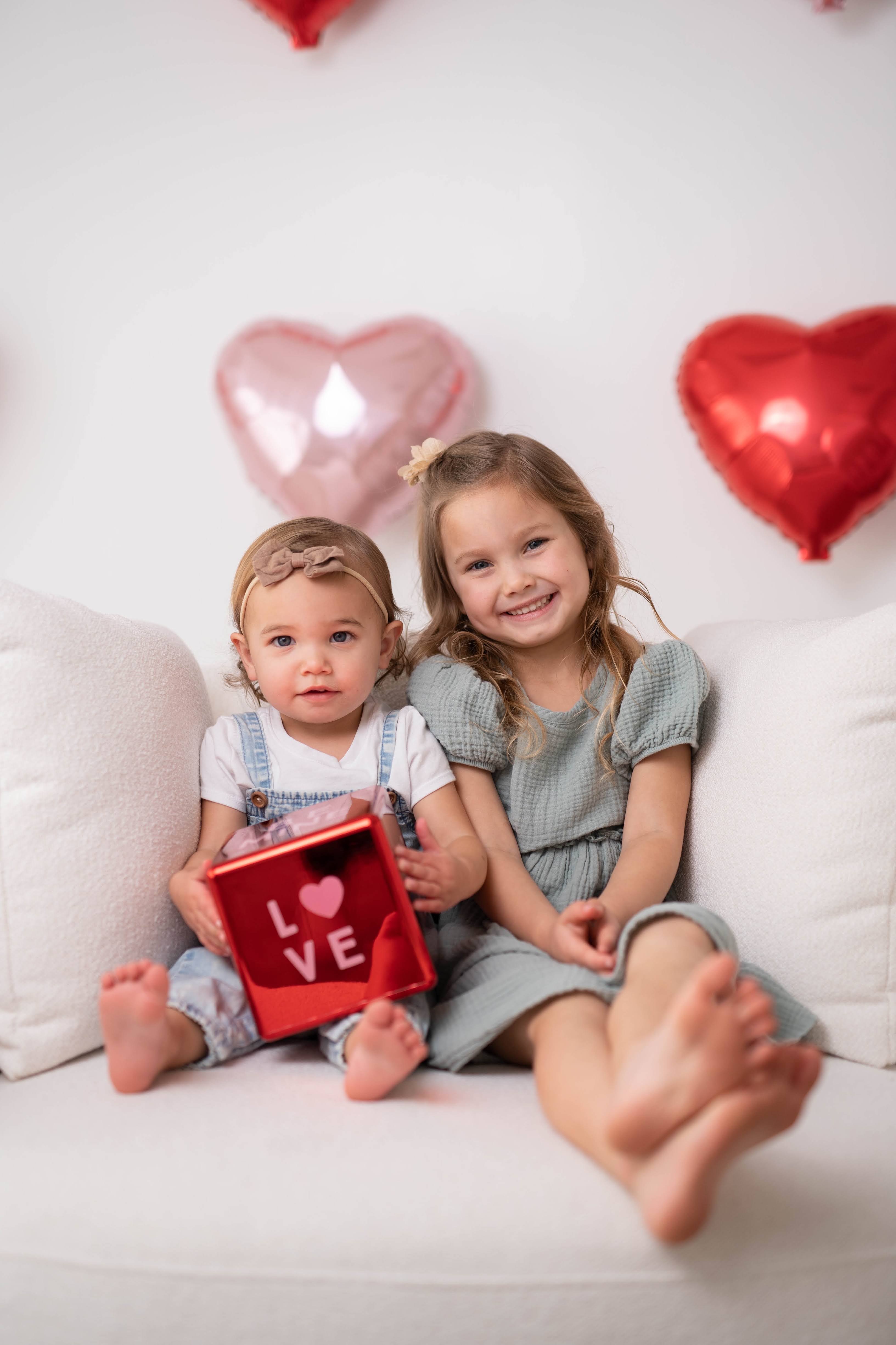 Two sisters sitting with heart balloons during a Vacaville family and kids photography session.